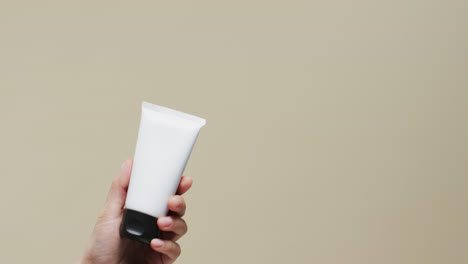 hand of woman holding tube with cream on beige background with copy space, slow motion