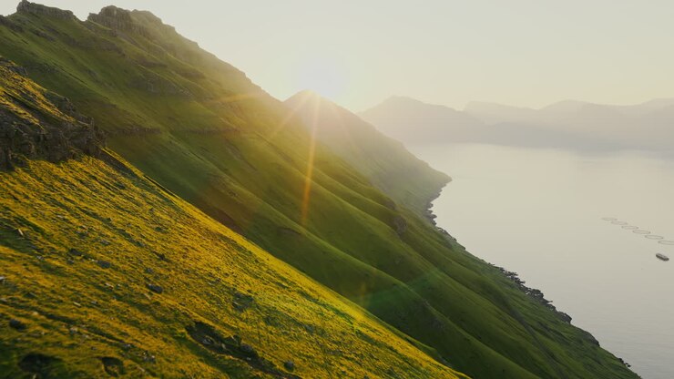 Sunlight illuminating a steep green mountainside overlooking a serene fjord