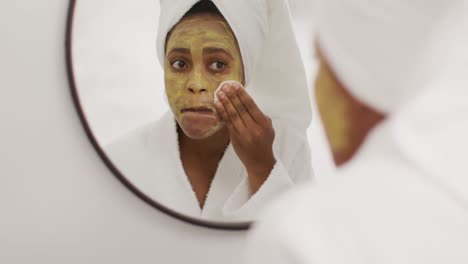Happy-african-american-woman-cleaning-beauty-mask-in-bathroom