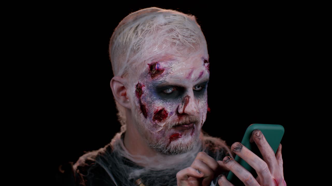 feliz emocionado hombre siniestro halloween zombi uso de teléfono inteligente celebrando la lotería ganar, éxito suerte