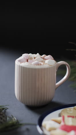 vertical video of mug of chocolate with marshmallows, cookies, copy space on black background