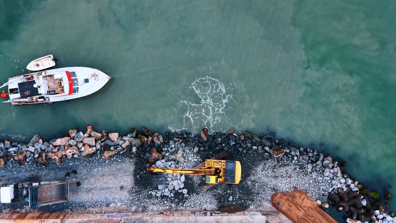 Vista aerea dall'alto di uno schizzo d'acqua durante la costruzione costiera. Escavatore al lavoro sulla riva con un grande schizzo bianco nell'acqua causato dal posizionamento di rocce pesanti.