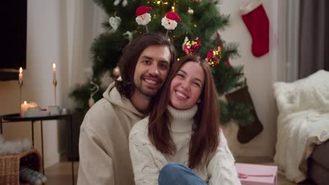 Retrato-De-Una-Pareja-Feliz,-Un-Chico-Moreno-Está-Sentado-Con-Su-Novia-Con-Un-Suéter-Blanco-Y-Adornos-De-Año-Nuevo-Cerca-De-Un-árbol-De-Año-Nuevo-Decorado-Con-Juguetes-De-Año-Nuevo-En-Una-Acogedora-Habitación-En-Invierno.