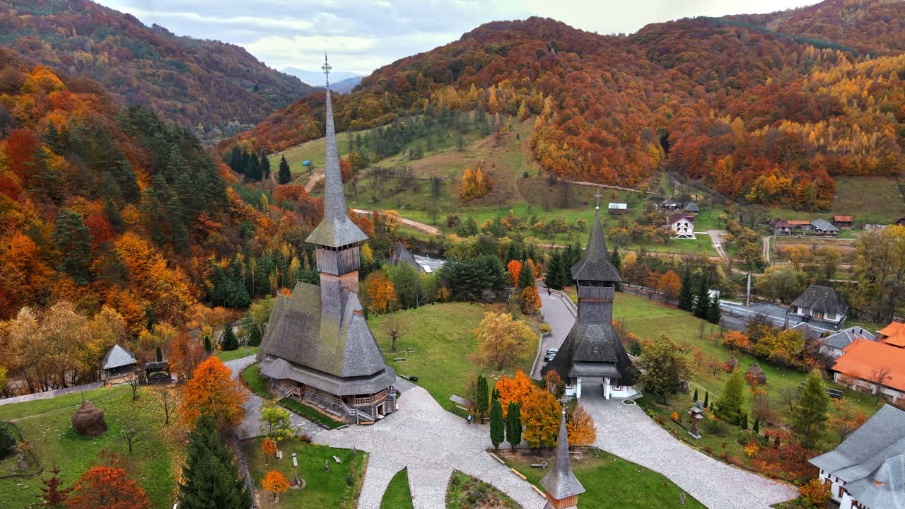Aerial drone view of the Barsana Monastery, Romania. Main church and other buildings, visitors, hills covered with yellowing forest around