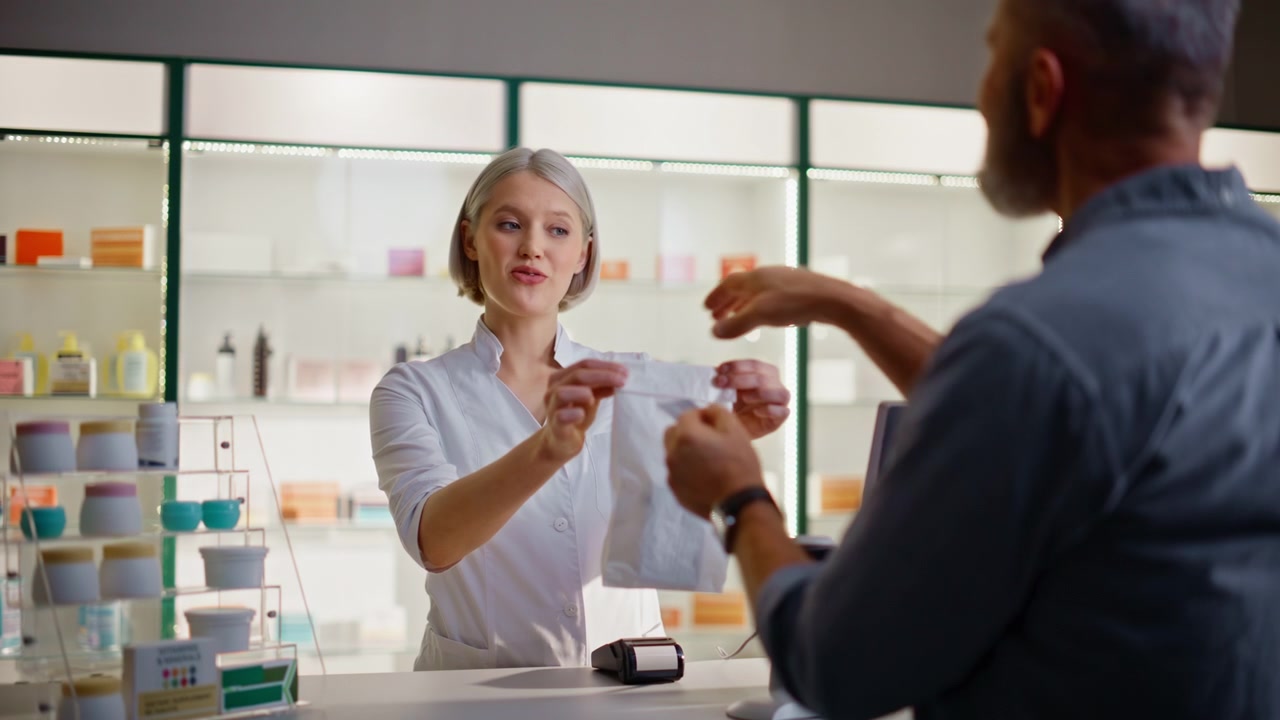 Farmaceut taster på terminalmaskine, udfører betaling og pakker piller ved kassen.