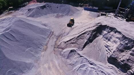 Yellow loader excavator on a granite quarry. Large mounds of rubble. asphalt plant. Aerial flight over crusher in granite quarry