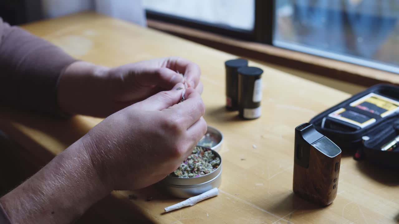 Male Hands Rolling Cannabis Cigarette (Joint) In Rolling Paper. closeup shot