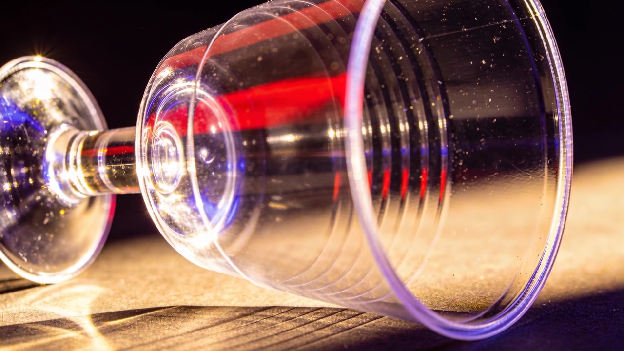 Revealing clear wine glass lying on wood table, colored lights shifting and dust catching light