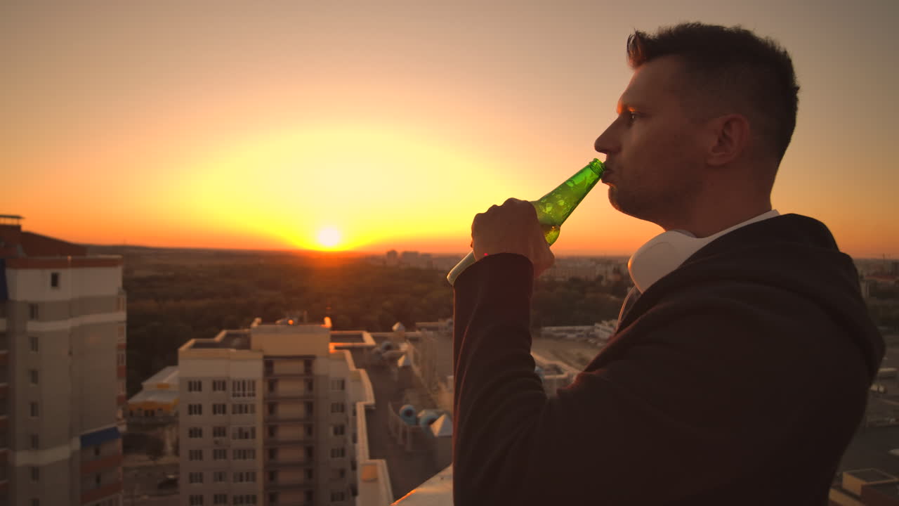 un hombre bebe cerveza de pie en el techo y contempla el mundo. mira la vista de la ciudad al atardecer desde una altura. el techo de un rascacielos.