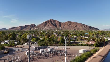 drone ascending over canal showing camelback mountain with houses, trees, and cellphone towers
