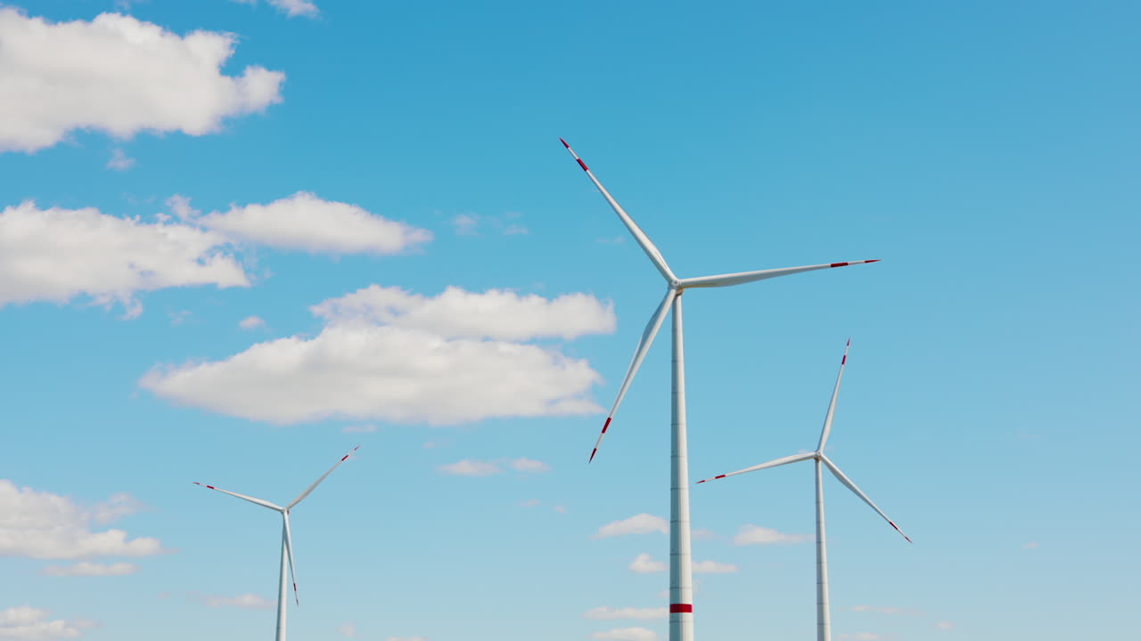 White turbines with red lines rotate in the wind. Energy production concept. Blue sky at backdrop.