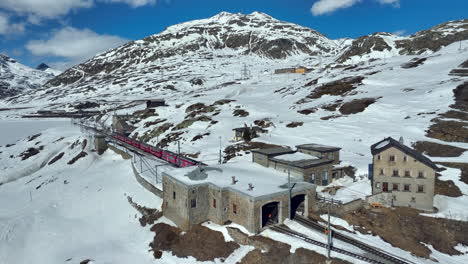 Tren-De-Pasajeros-Rojo-Acelerando-Desde-La-Estación-De-Tren-Bernina-Ospitz-En-Un-Día-Soleado