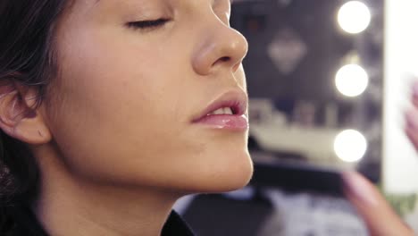 process of make up artist's hand applying concealer on t-zone of a beautiful attractive girl's face in a beauty studio.