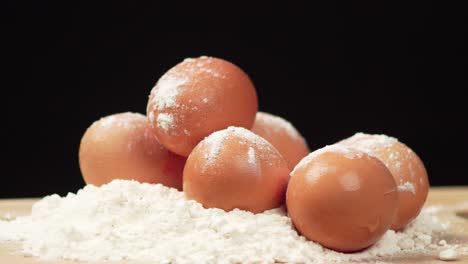 Close-up-of-the-eggs-in-flour-on-a-wooden-board-rotating-on-a-black-background