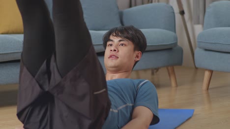 강한 운동선수 셔츠를 벗고 스포츠 옷을 입은 아시아인 남자가 집에서 복부 운동을 하고 있습니다.