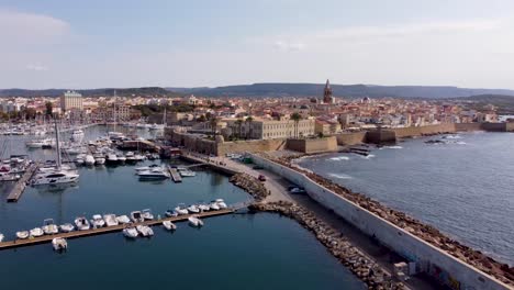 Seitlicher-Drohnenclip-über-Einem-Wellenbrecher-Und-Einem-Jachthafen-Mit-Luxuriösen-Yachten-In-Der-Altstadt-Von-Alghero-Auf-Sardinien,-Italien