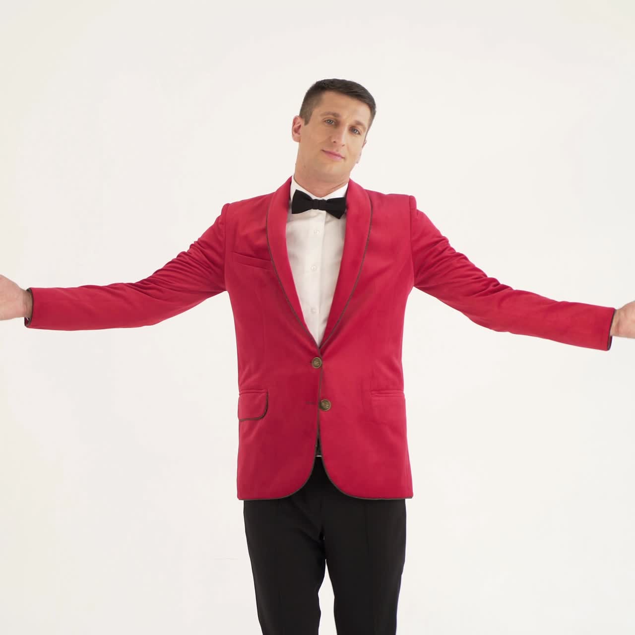 showman in a red jacket with a bow tie is circling around himself with openarmed hands in different sides on a white background