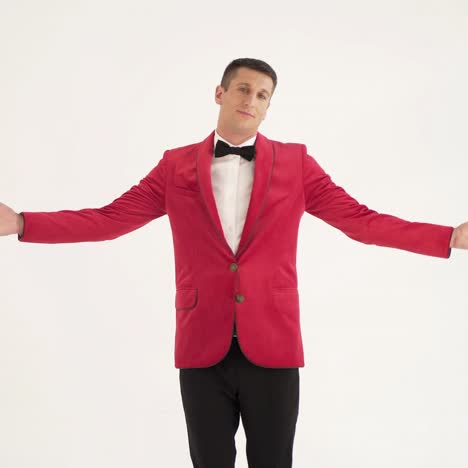 ein schauspieler in einer roten jacke mit einer fliege kreist mit offenen händen auf verschiedenen seiten auf einem weißen hintergrund um sich herum