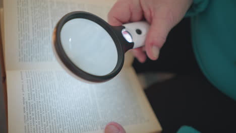 close-up of elderly woman holding magnifying glass over book text. focus on magnifier highlighting small print in book, with soft lighting accentuating details in hands, glasses, and text