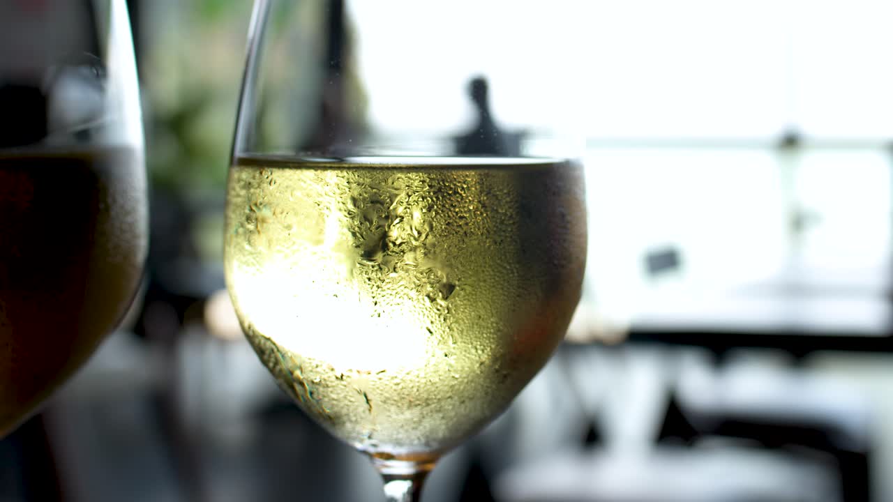 Primo piano di un bicchiere di vino bianco freddo con condensa su un patio esterno.