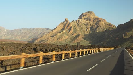 driving on a highway with a roadside fence going towards the mountain during sunset, pov