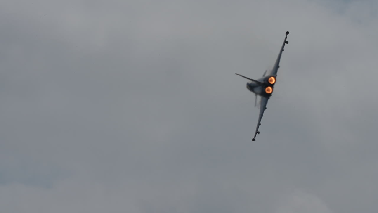 Military jet aircraft turning in slow motion with visible afterburner flames coming from engines against cloudy sky