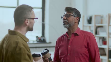middle-aged indian man talking with colleague on coffee break in office