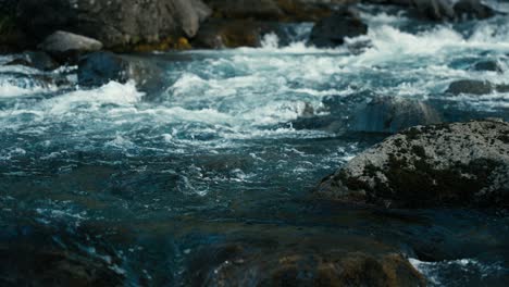 close up of crystal clear blue water flowing down a river and splashing over rocks