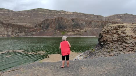 senior, female pointing to the cliffs surrounding alkali lake in northern washington state on a cloudy, breezy afternoon