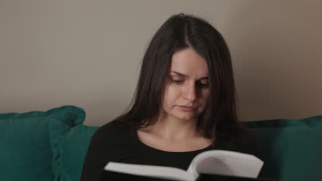 a woman, sitting on the sofa, absorbed in the pages of a book - close up