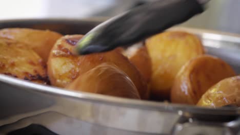 frying golden brown potatos with skins in a silver pan using tongs