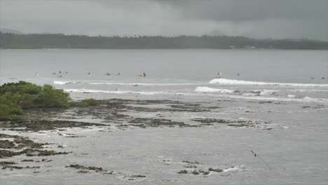 Das-Ruhige-Meerwasser-Mit-Menschen,-Die-Es-Genießen,-Unter-Dem-Bewölkten-Himmel-Durch-Die-Wellen-Zu-Schwimmen---Weitwinkelaufnahme