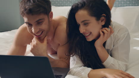 Couple-surfing-internet-computer-in-bed.-Beautiful-couple-looking-laptop-screen.