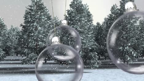 animación de bolas de navidad colgando sobre la nieve que cae y los árboles en el paisaje de invierno.