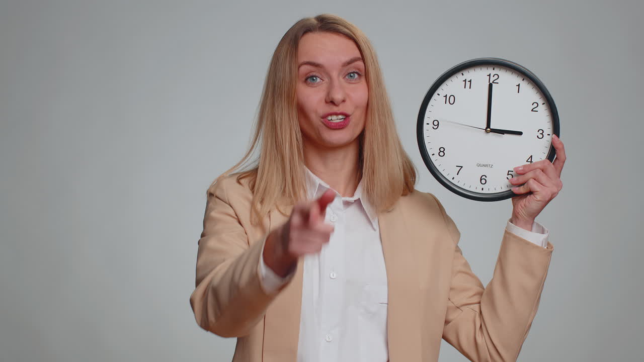 Business woman showing time on wall office clock ok thumb up approve pointing finger at camera
