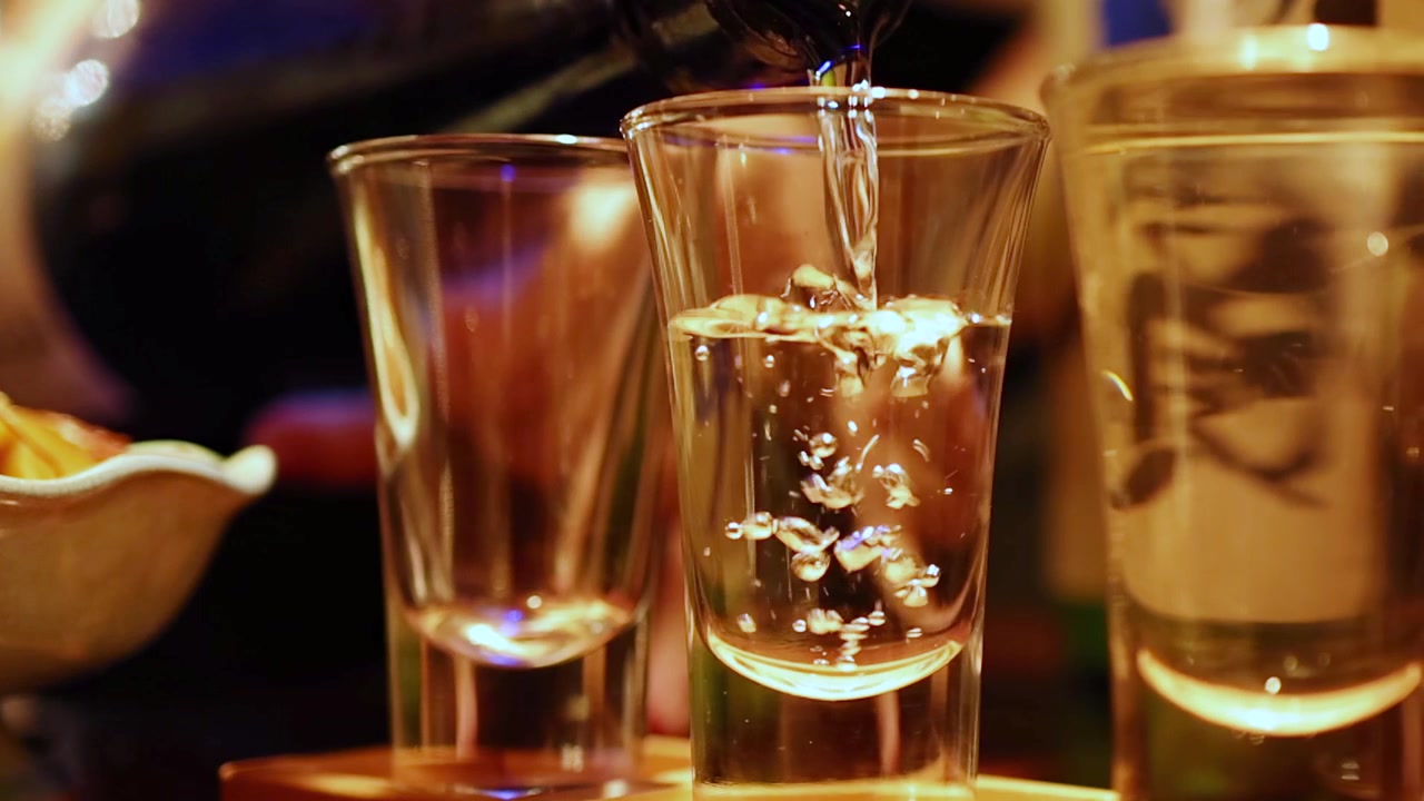 Sake trasparente versato in un piccolo bicchiere in un bar di un ristorante di Tokyo con luci soffuse
