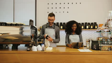 caucasian barista with beard and african young woman working in trendy coffee shop