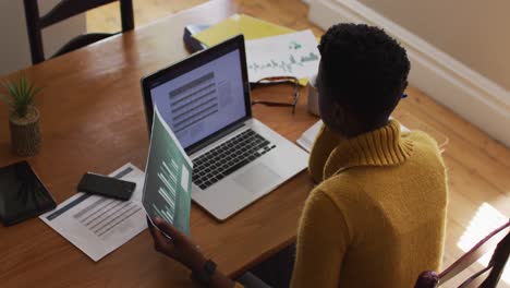 overhead view of african american woman reading document and using laptop while working from home