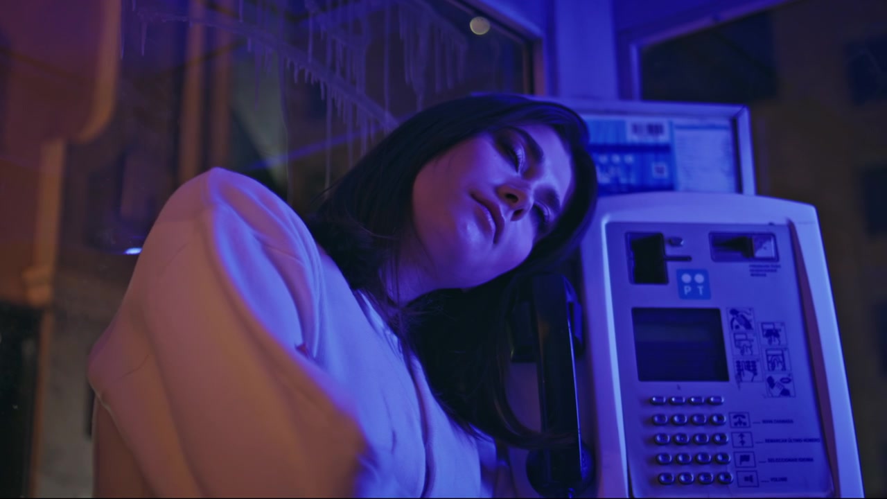 Primo piano di una donna in una cabina telefonica. Ritratto di ragazza appoggiata a una cabina telefonica con bagliore neon notturno