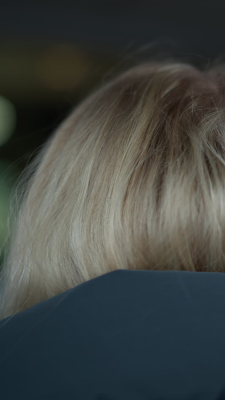 vista trasera de la cabeza de la dama con el cabello dorado con capucha, caminando en un espacio débilmente iluminado, la figura borrosa se mueve en el fondo, creando una atmósfera de mal humor con una iluminación suave