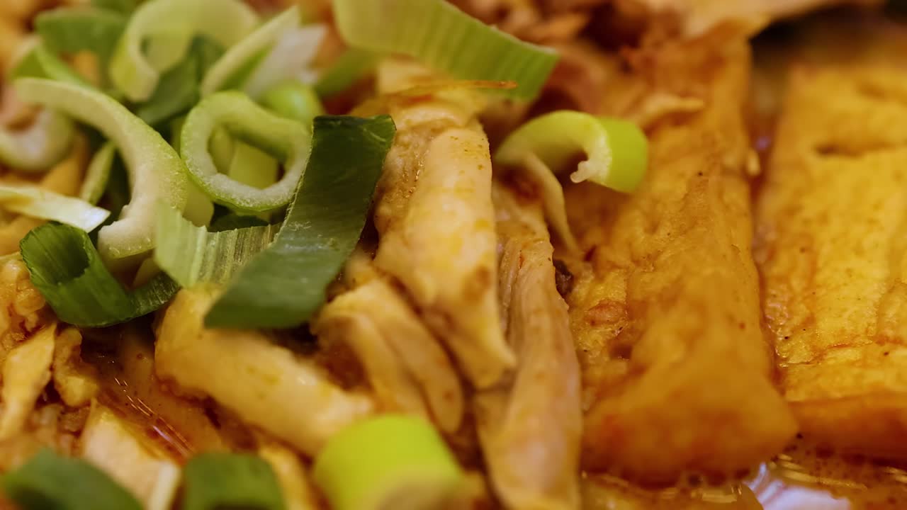 A detailed view of tofu slices topped with green onions in a rich, savory broth.