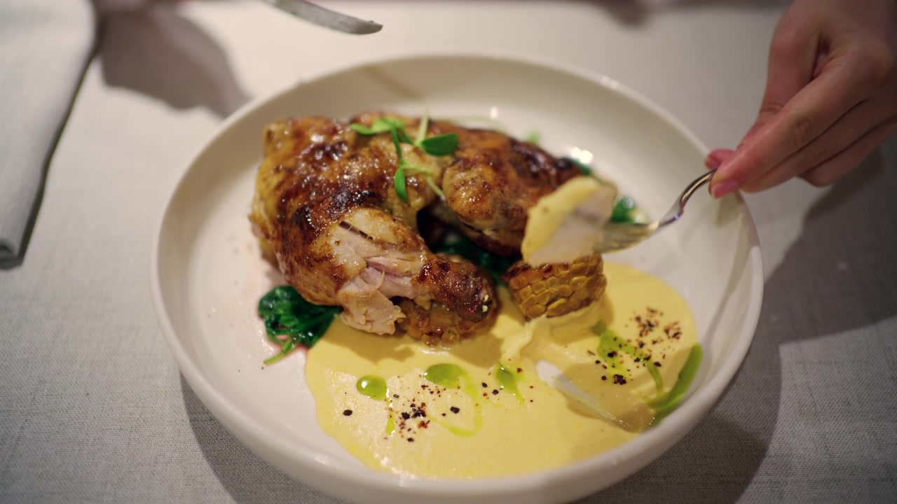 Close up of a woman using a knife and fork while adding or adjusting fresh microgreens on a roasted chicken dish