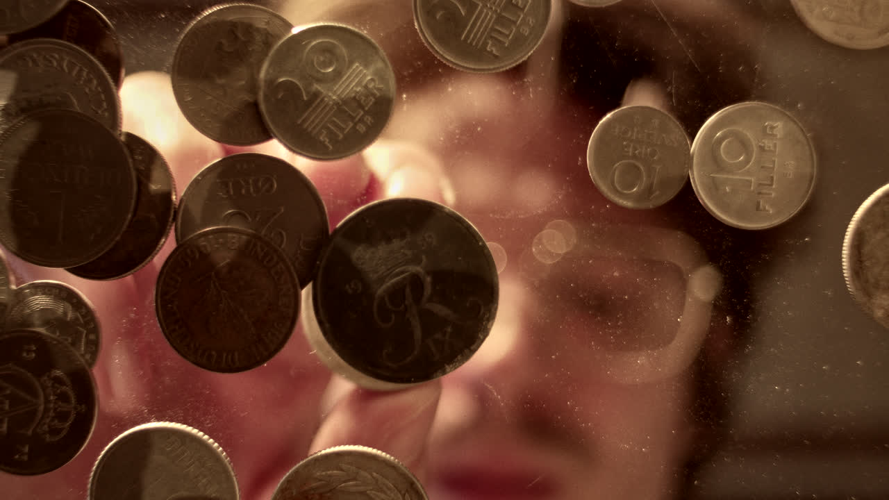Old coins on a reflective surface with a blurred human reflection underneath
