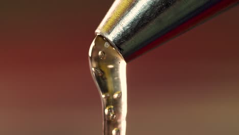 un primerísimo plano de macro que gotea pegamento caliente de la boquilla metálica
