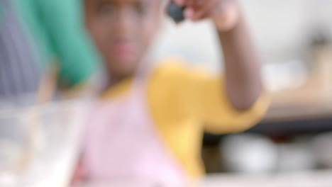 Happy-african-american-daughter-eating-blueberries-with-mother-in-kitchen,-slow-motion