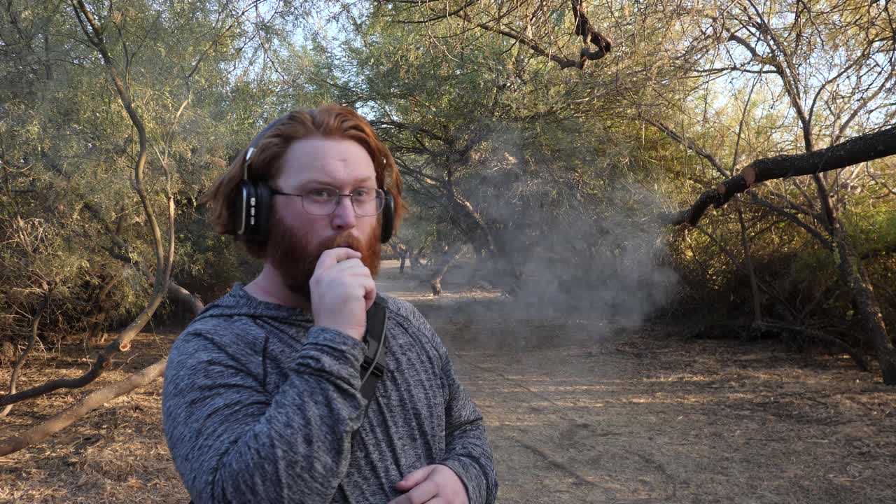 Red haired man vaping while listening to music with headphones.