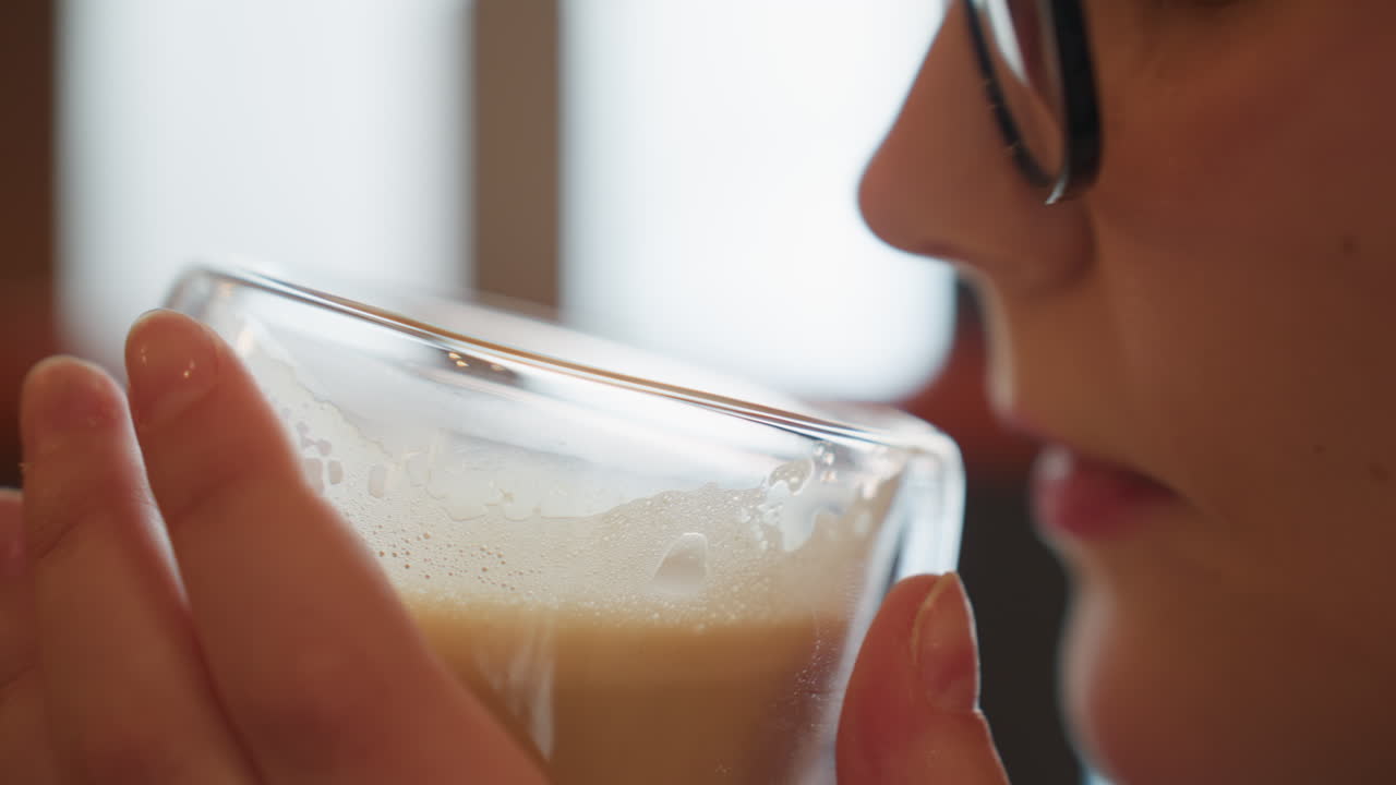 close up of woman holding transparent glass of milkshake with both hands as she prepares to take sip, soft natural light and blurred background