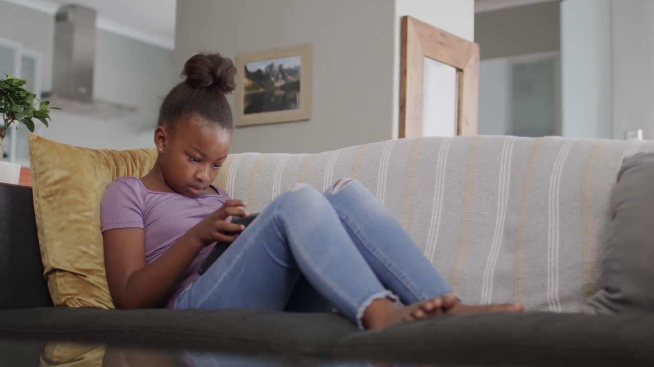 African american girl sitting on sofa and using tablet, slow motion, unaltered