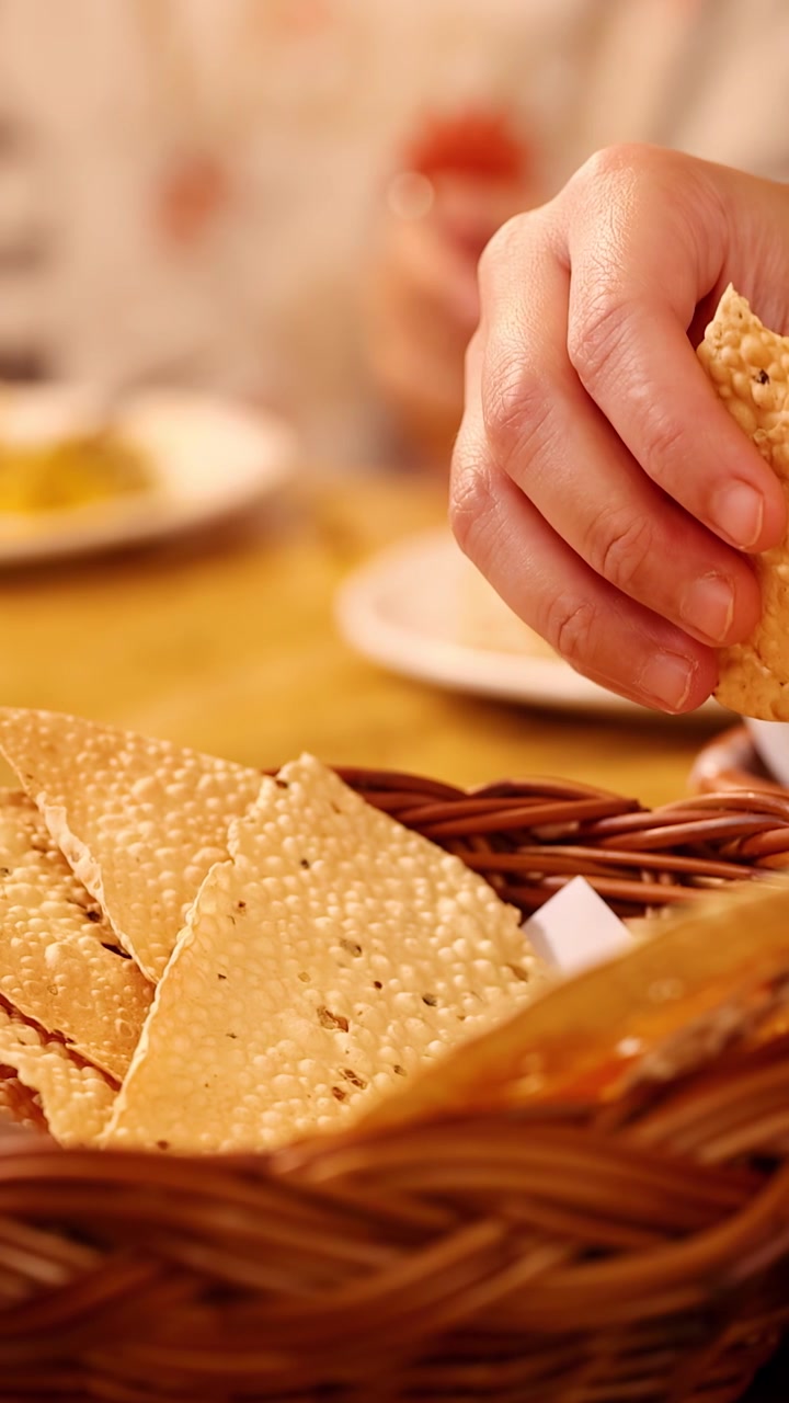 Close-up shot of hands breaking crispy papadum bread over a basket in warm restaurant lighting.