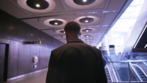 Young Businessman Wearing Suit Commuting To Work Getting Off Escalator At London Underground Station Using Mobile Phone Shot In Real Time